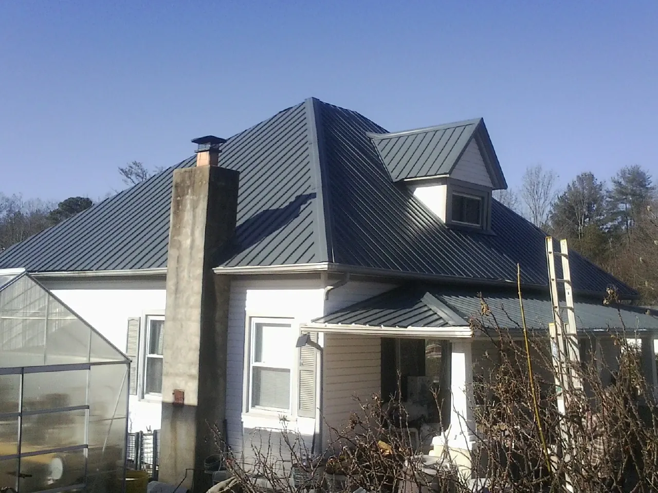 Dark blue standing seam metal roof on a white farmhouse with dormer — Slate & Tile Roof Repair by Roofing Brothers in Garden Valley
