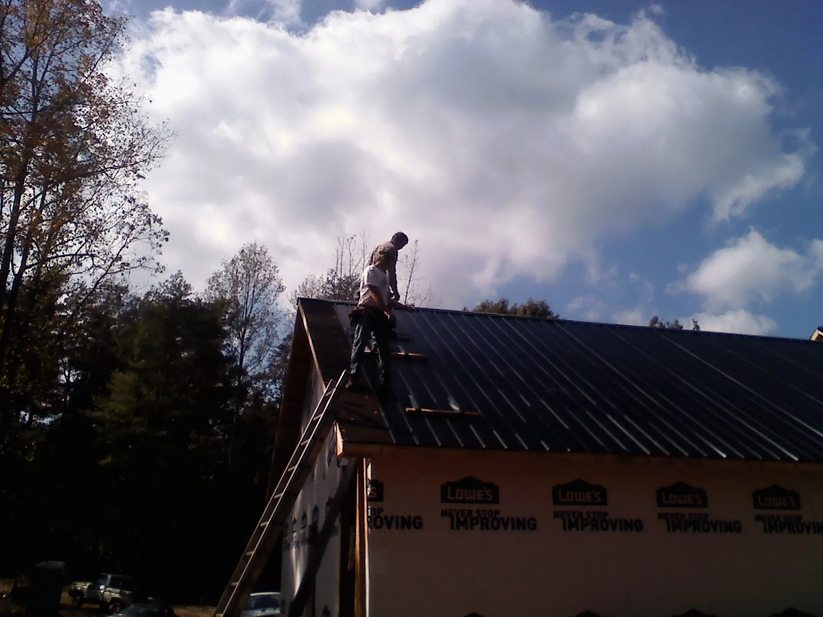 Roofer fastening dark metal panels high against a cloudy sky, from a Roof Inspection job in Garden Valley