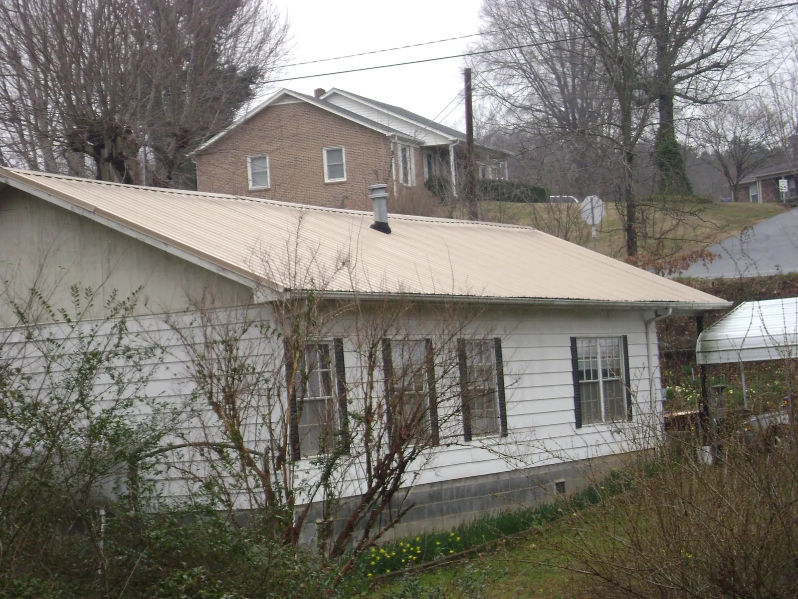Tan metal roof on a white sided house set into a hillside — Commercial Roofing by Roofing Brothers in Garden Valley